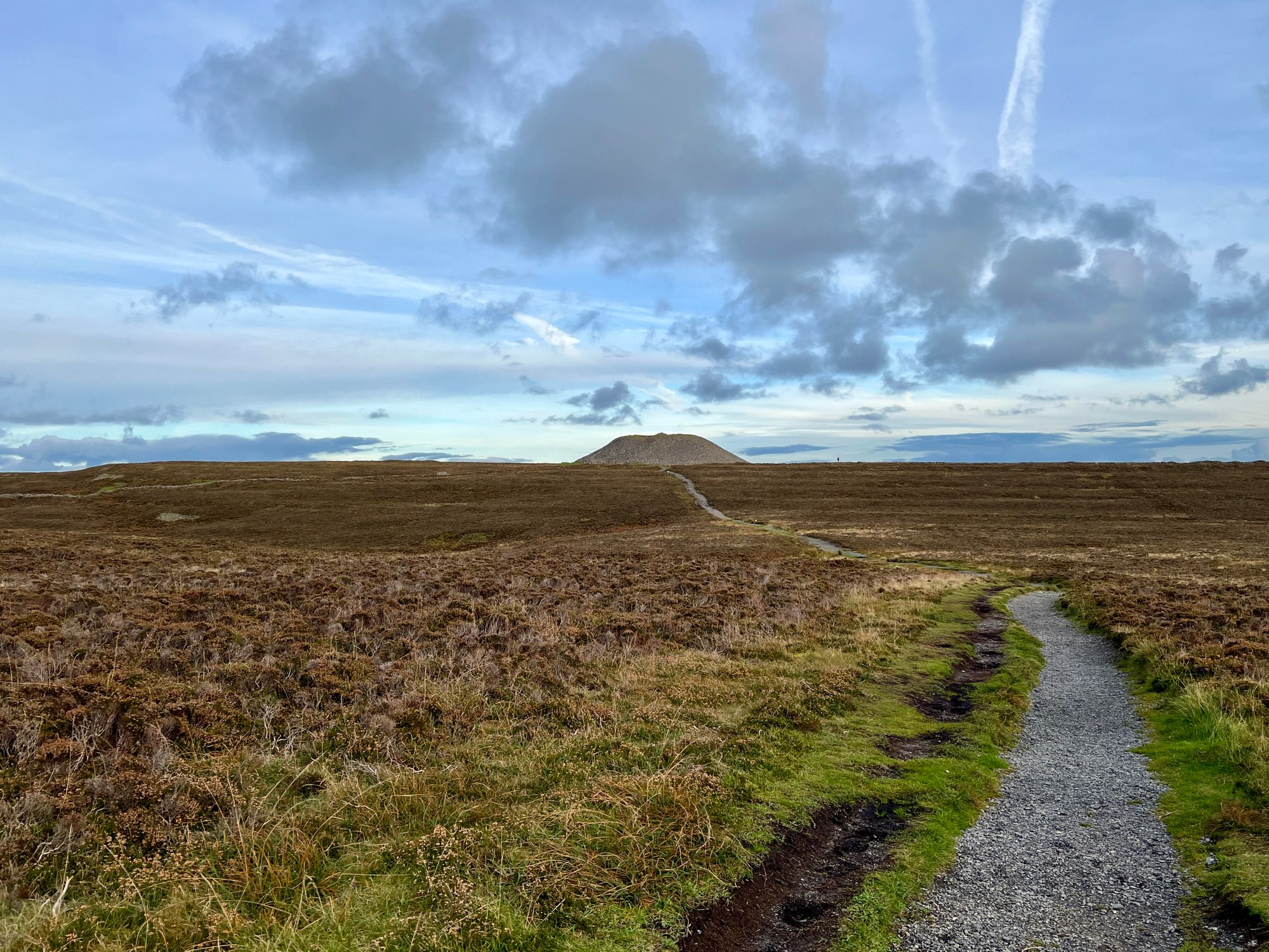 photo of Queen Maeve's Tomb, a stone megalith far off in the distance under a dramatic sky