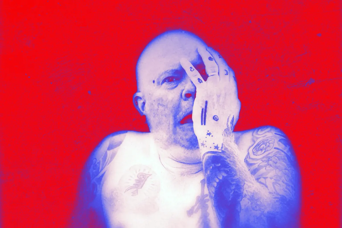 Highly distressed photograph of a purple bald guy covering his face with one hand in horror against a bright red background.