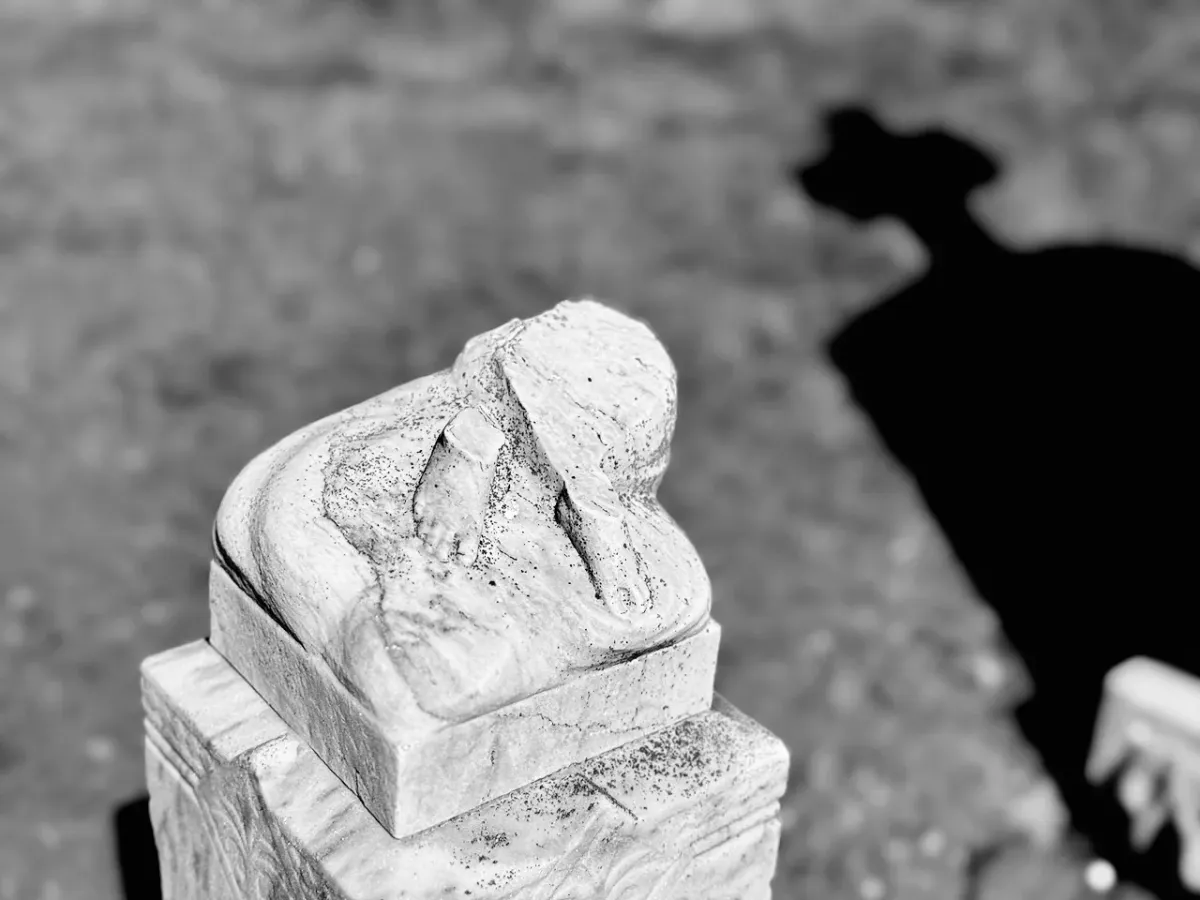 Black and white photo of two concrete feet atop a gravestone. The body that once stood there is missing.