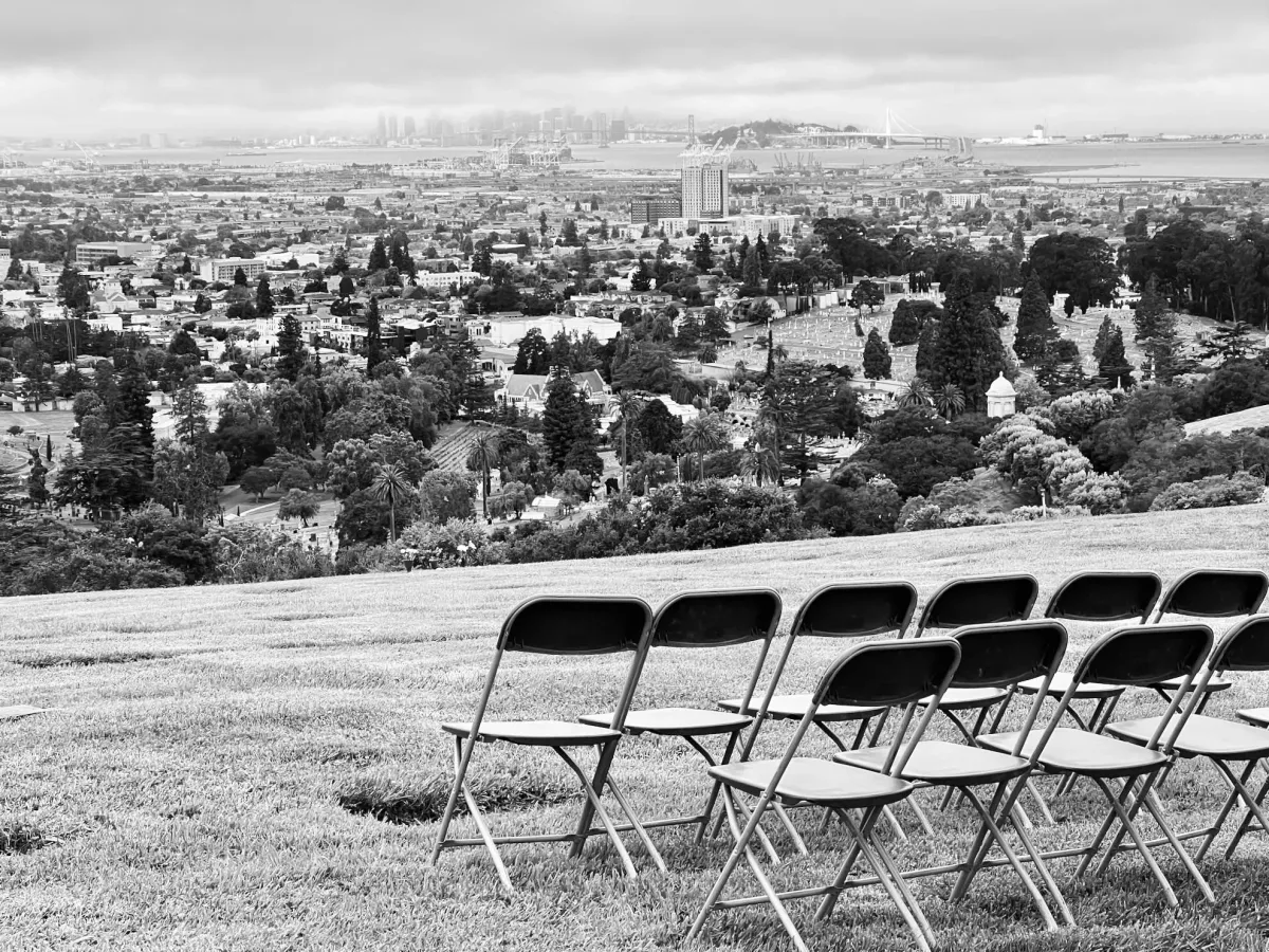 Black and white photo of two rows of folding chairs on a hill overlooking a distant city.