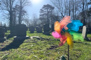 photograph of a colorful spinning pinwheel in a cemetery with gravestones in the background