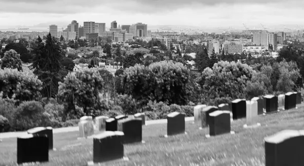 Black and white photo of a row of gravestones on a hill overlooking a city skyline.